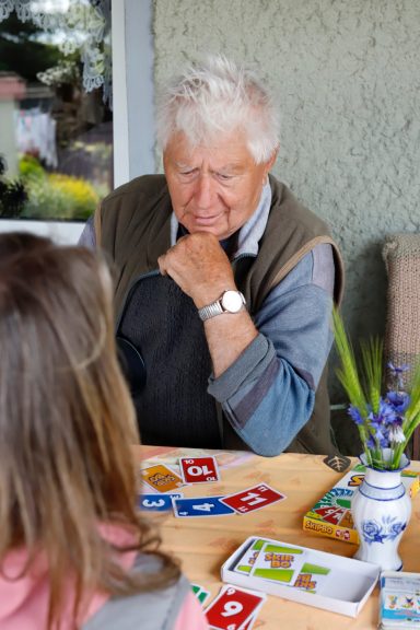 Alltagsbegleitung mit Herz Ein älterer Mann spielt ein Kartenspiel mit einem jüngeren Mädchen. Tisch mit Karten sichtbar.