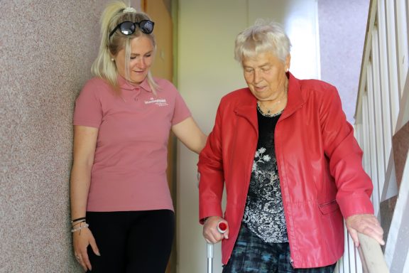 Alltagsbegleitung mit Herz Junge Frau hilft älterer Frau beim Treppensteigen. Beide lächeln.