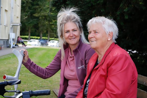 Alltagsbegleitung mit Herz Zwei Frauen sitzen im Freien auf einer Bank, lächeln und genießen die Zeit zusammen.
